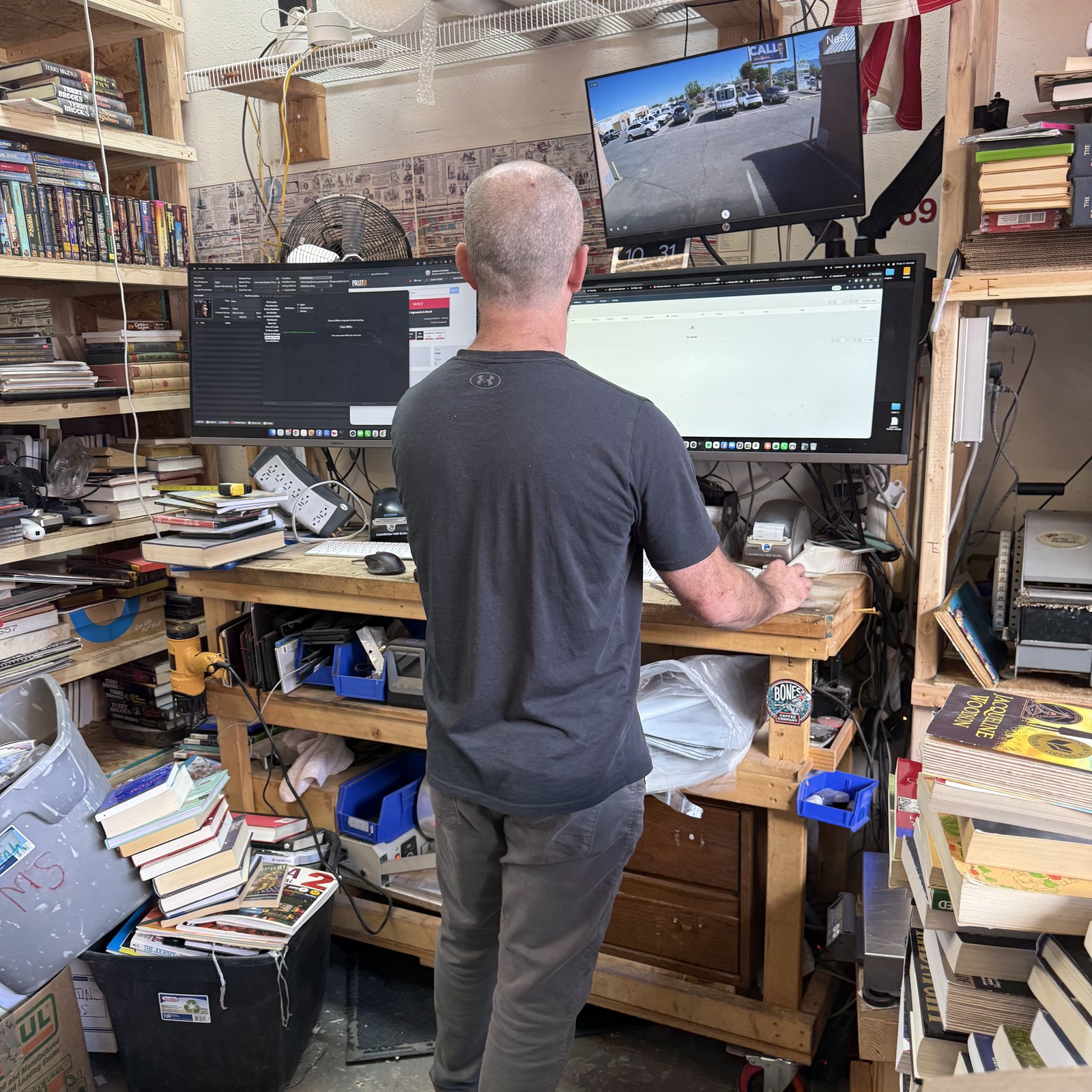 Josh Eldred at the sorting workstation in the SellBooksABQ warehouse — books on shelves, monitors up, the real intake setup.