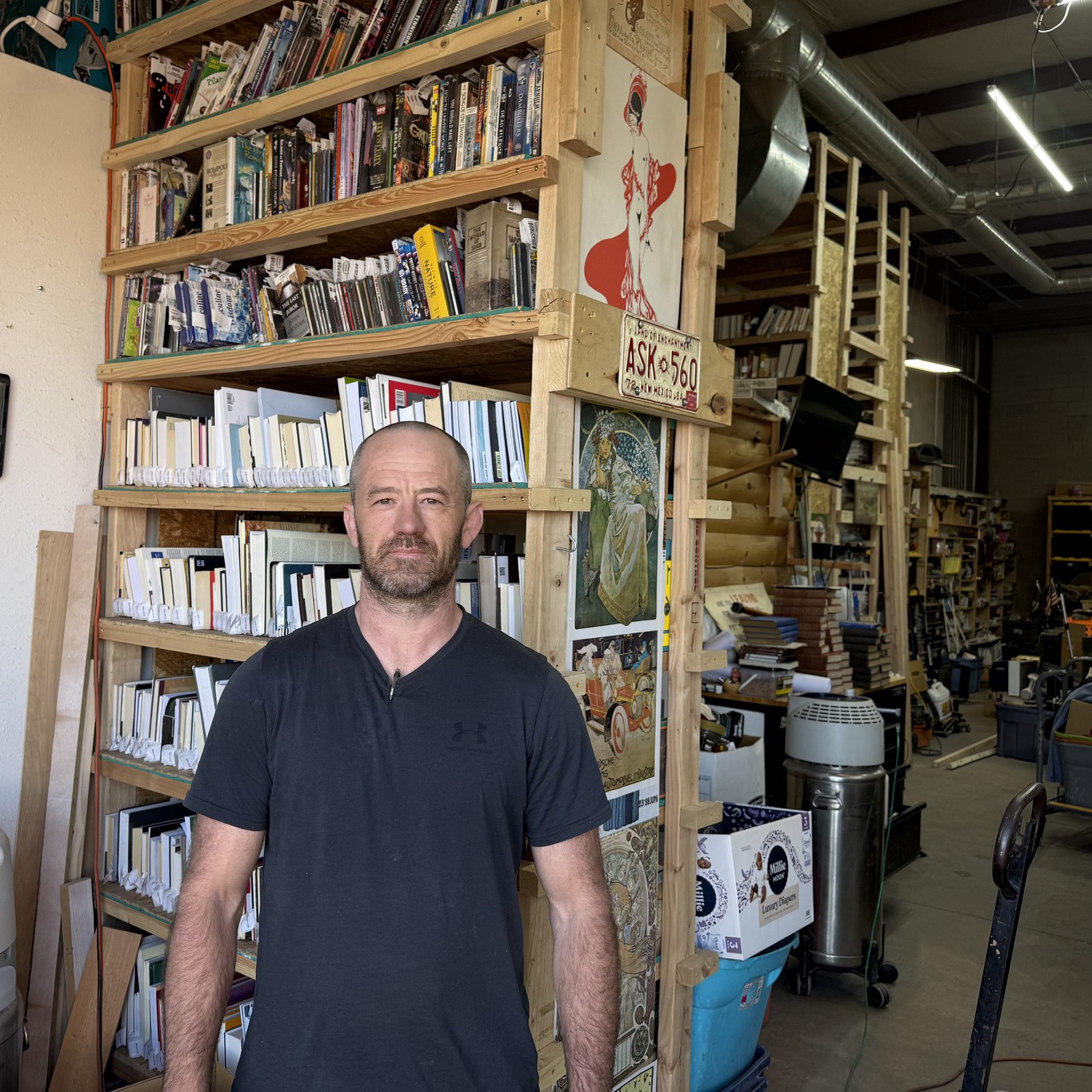 Josh Eldred, owner of SellBooksABQ, standing in front of a full wall of books at the warehouse in Albuquerque.