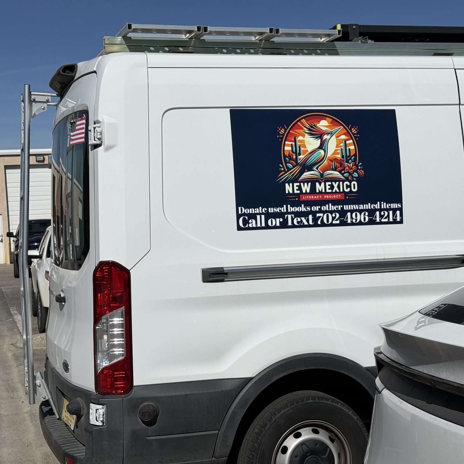 White Ford Transit van with a New Mexico Literacy Project magnetic sign on the side panel — a roadrunner illustration, the phone number, and 'Donate used books or other unwanted items'.
