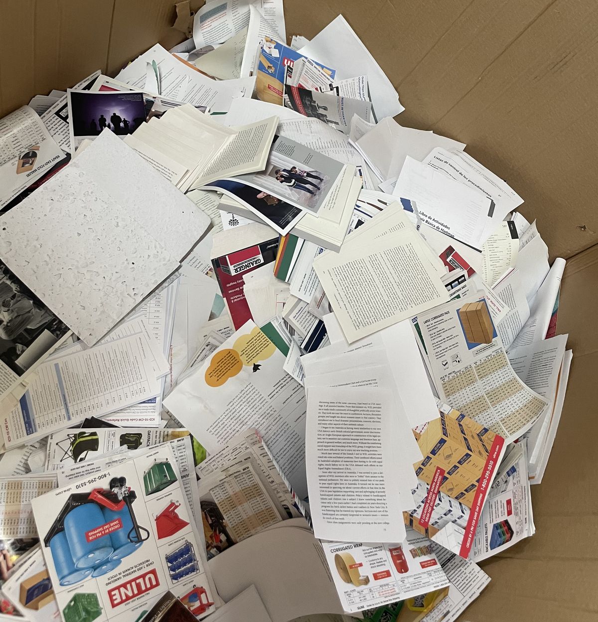 Inside a gaylord box full of loose paper from cut-up books and catalogs — mixed book pages, supply catalogs, and overprinted reference material ready for the paper recycler.