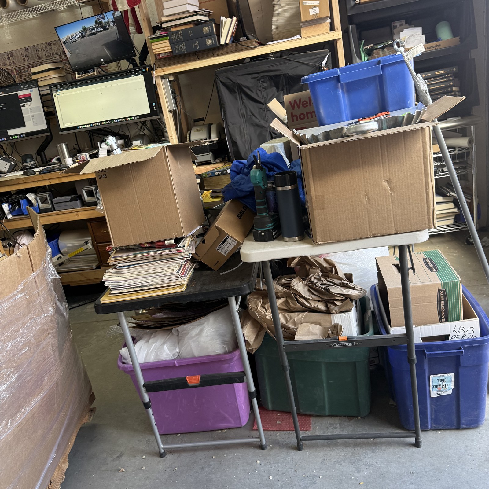 Staging area inside the SellBooksABQ warehouse at Unit A-2 in Albuquerque — cardboard boxes, storage bins, and sorting tables loaded with books fresh from an estate pickup.